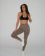 Woman wearing a black sports bra and brown leggings on a white background